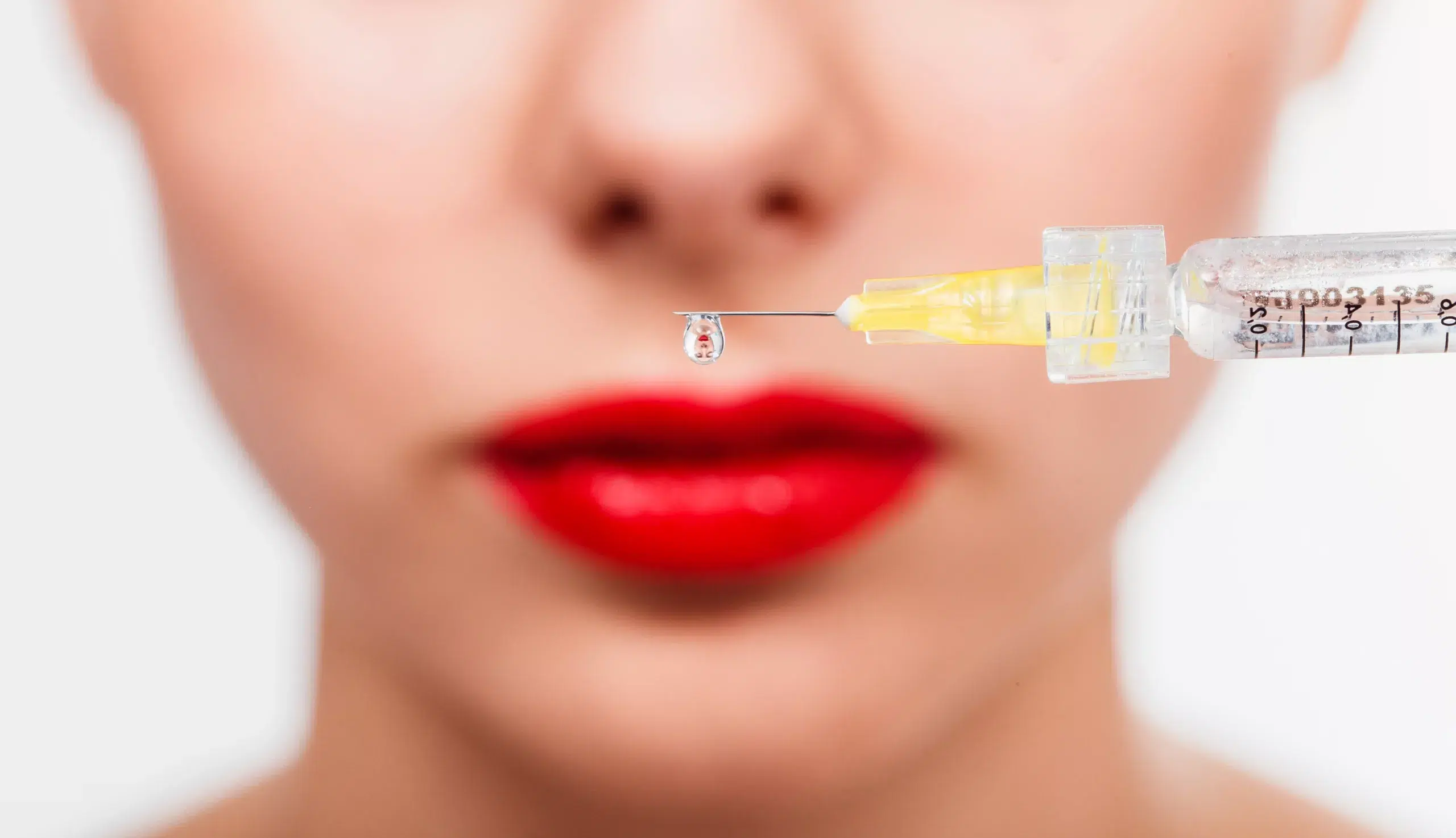 A drop of preparation hangs from the needle of the syringe against the face of the patient. Macro close upA drop of Botox hangs from the needle of the syringe against the face of the patient. Macro close up de vraies innovations dans les injections d'acide hyaluronique en Médecine Esthétique Clinique Rivoli Massena 2
