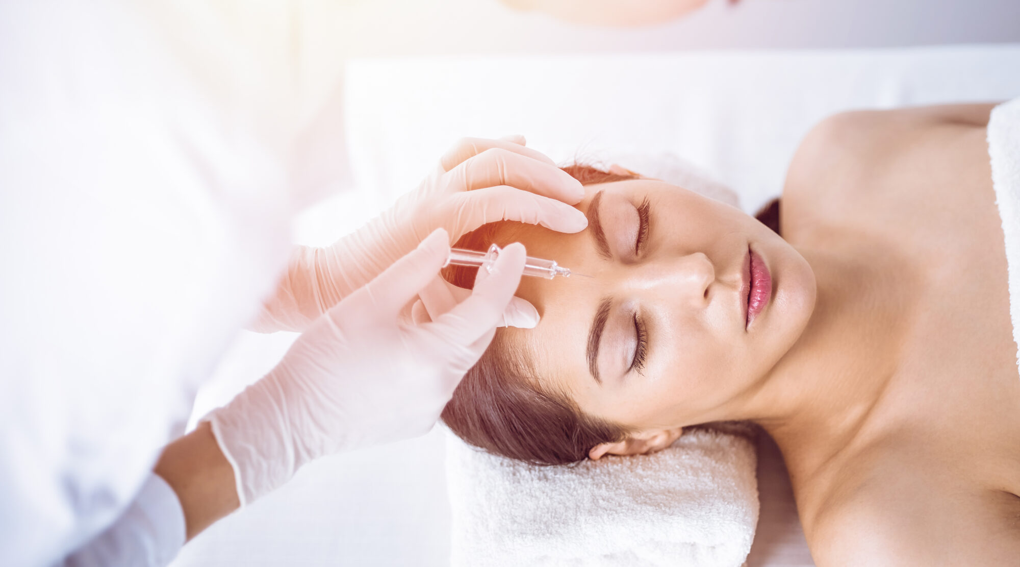 Beautician doing beauty procedure with syringe to face of young brunette woman in sunny spa center. Cosmetic medicine and surgery, beauty injections FAQ sur les injections d'acide hyaluronique en Médecine Esthétique Clinique Rivoli Massena 2